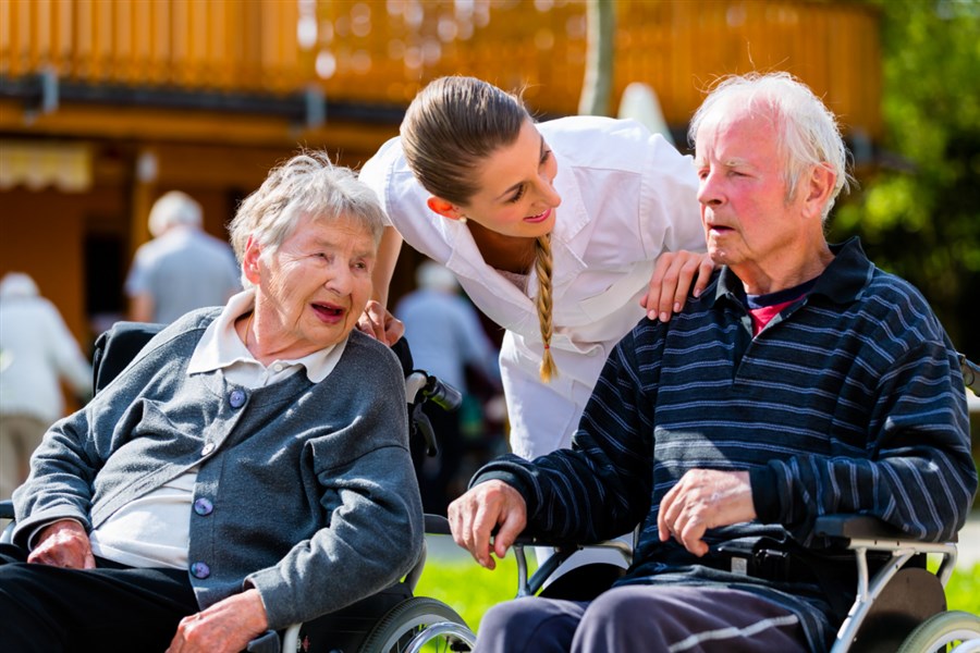 foto van een verpleegster bij een bejaarde man en vrouw in rolstoel